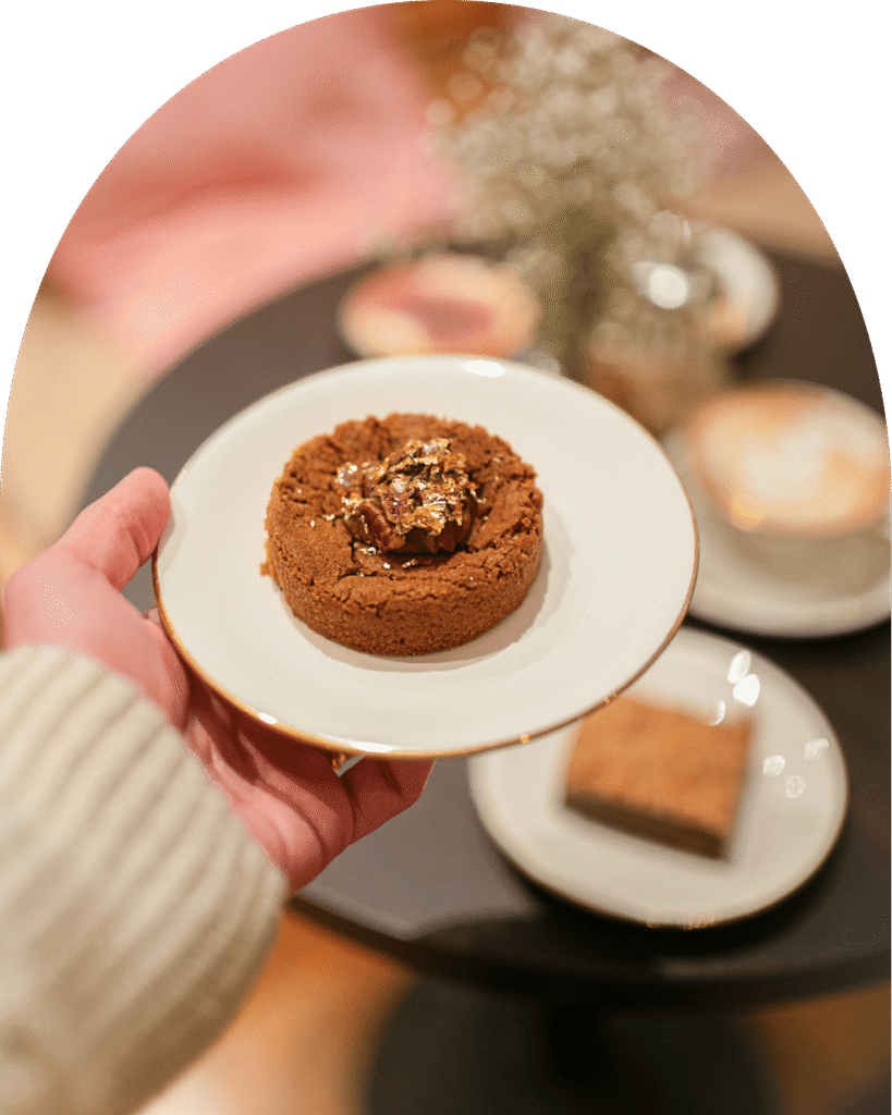Biscuit chocolaté garni de noisette et feuille d’or, tenu à la main dans le salon de thé La Tasse.