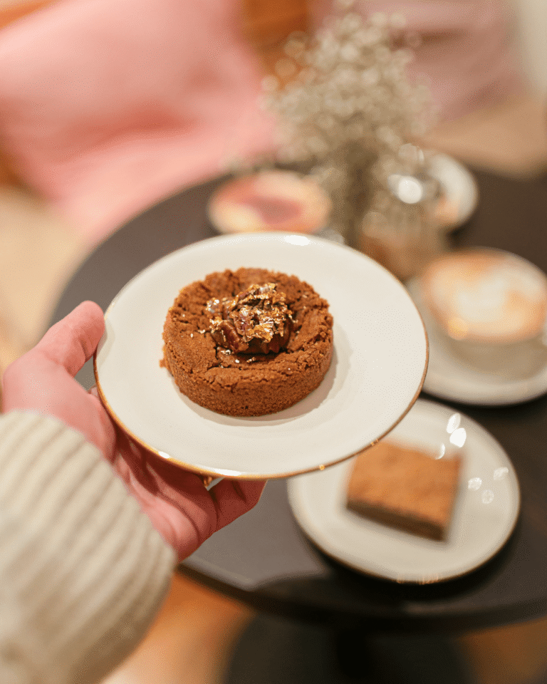 Cookie artisanal décoré d’éclats dorés, tenu à la main au café La Tasse à Uccle