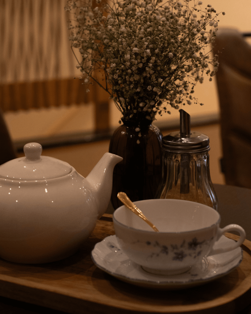 Théière blanche avec tasse vide et fleur séchée en fond, sur une table en bois chez La Tasse