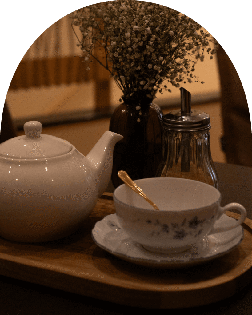 Tasse et théière en porcelaine blanche sur un plateau avec fleurs séchées et sucre, dans une ambiance douce.