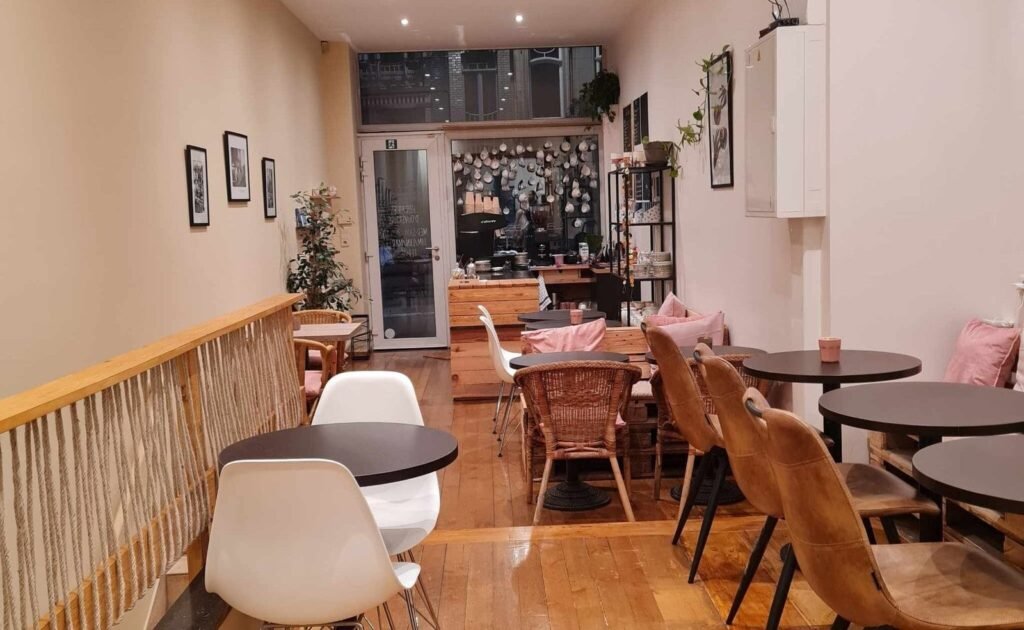 Vue intérieure du salon de thé La Tasse à Uccle, montrant un espace chaleureux avec chaises en rotin, tables en bois et décoration naturelle
