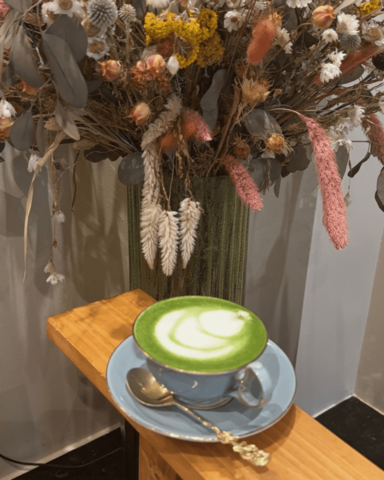 Matcha latte mousseux dans une tasse bleue, posé devant un grand bouquet de fleurs séchées colorées