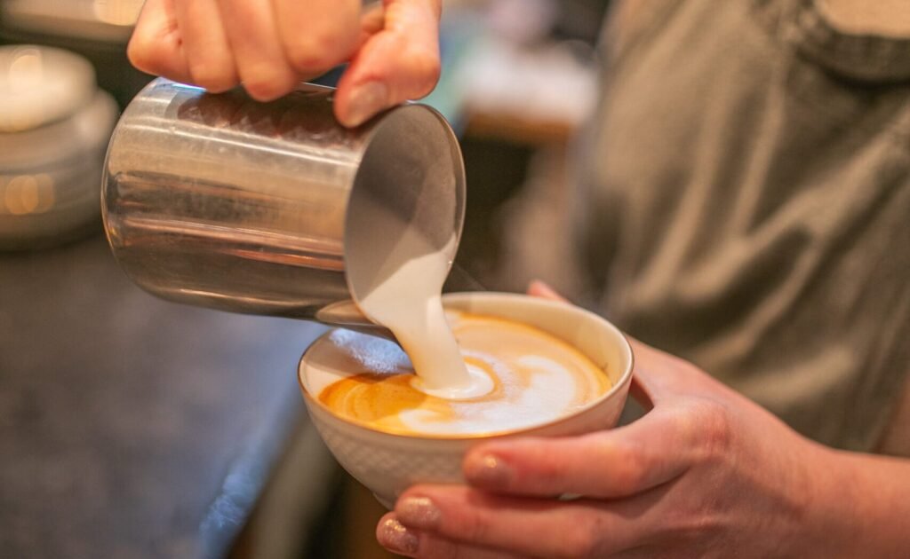 Gros plan sur la préparation d’un latte artisanal dans le salon de thé La Tasse à Uccle, avec mousse de lait versée à la main
