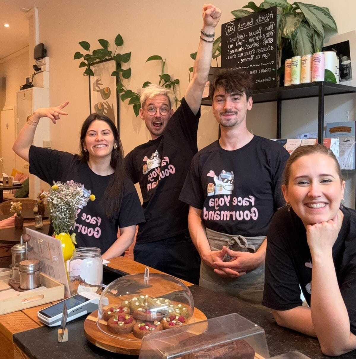 L’équipe du café La Tasse souriante derrière le comptoir, tous en t-shirts Face Yoga Gourmand, avec pâtisseries maison et ambiance chaleureuse